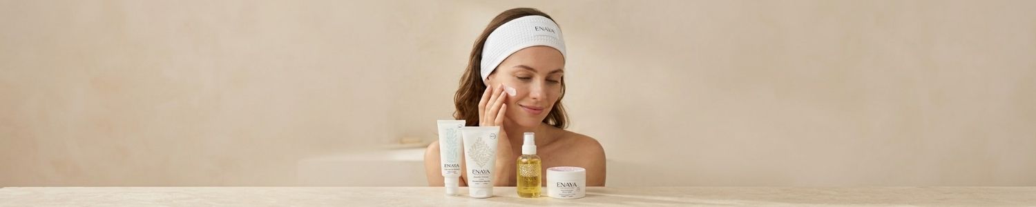 Banni&egrave;re soins du visage ENAYA, mod&egrave;le portant un bandeau blanc avec les produits de soin align&eacute;s sur une table dans une ambiance cocooning naturelle.